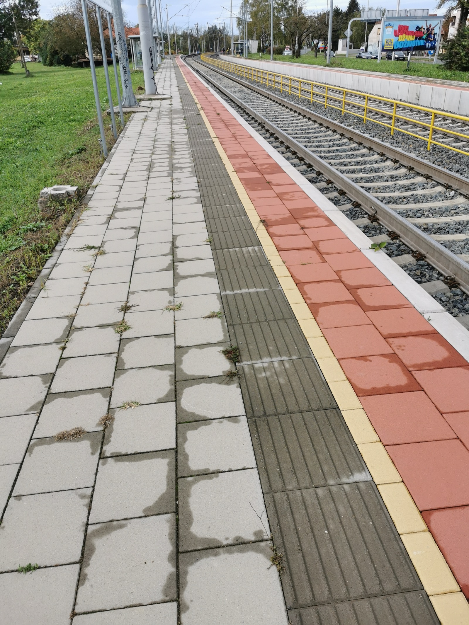 Yellow tactile paving with raised studs at the edge of a station platform, the warning surface blind and partially sighted people read underfoot.